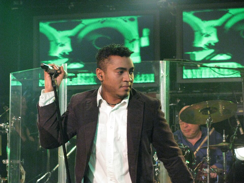 Michael Lascar singt am Mikrofon auf der Bühne, im Hintergrund Schlagzeug und grüne Bühnenprojektionen