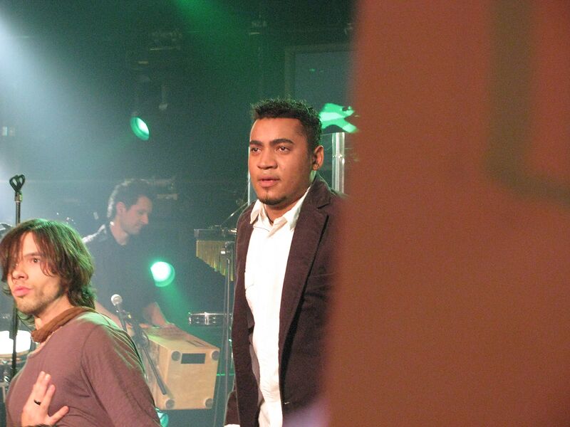 Michael Lascar im dunklen Jackett auf der Bühne mit Band in warmem Licht
